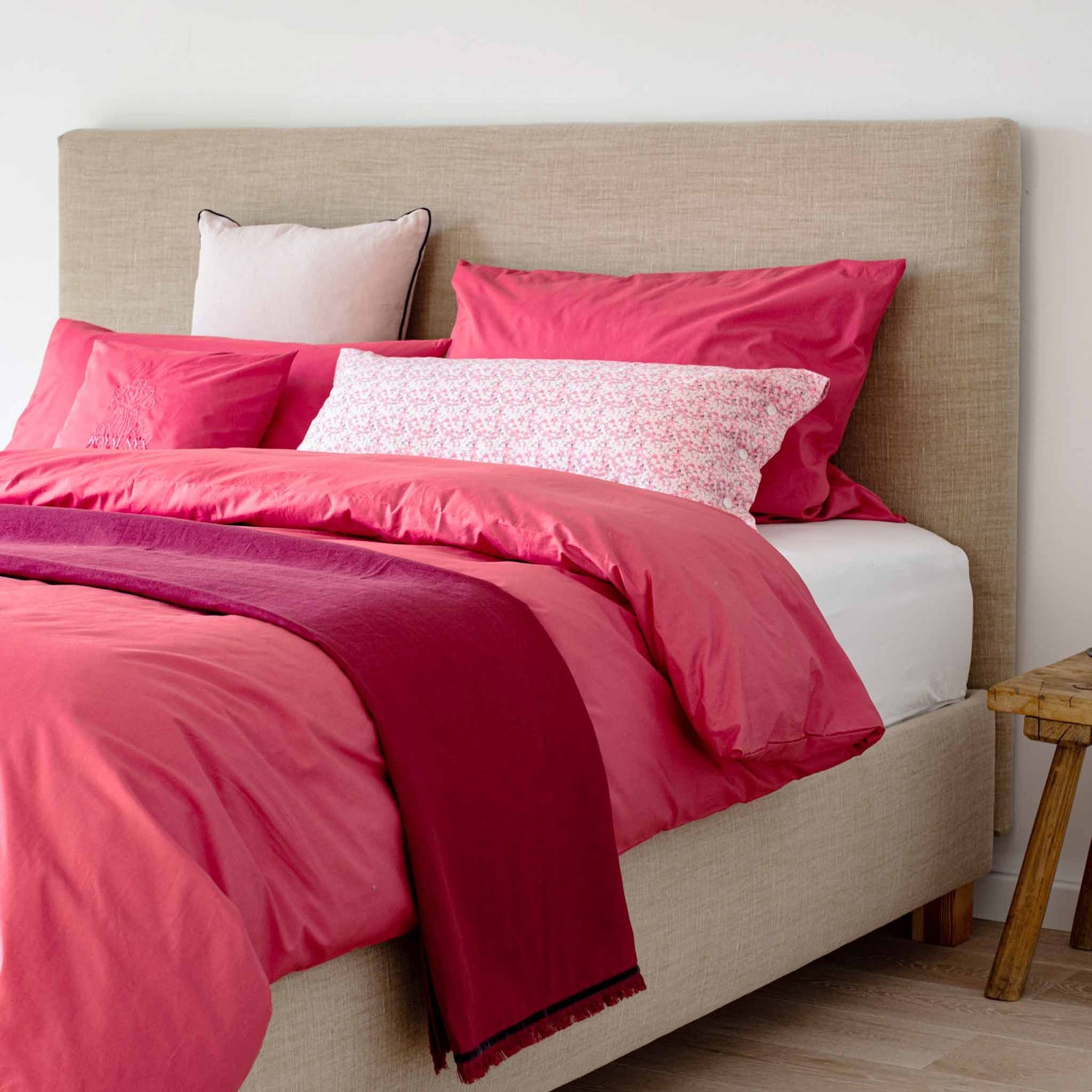 Polsterbett mit roter Baumwollbettwaesche und dunkelroter Leinendecke kontrastiert mit rosa geblümten Kissen 40x80