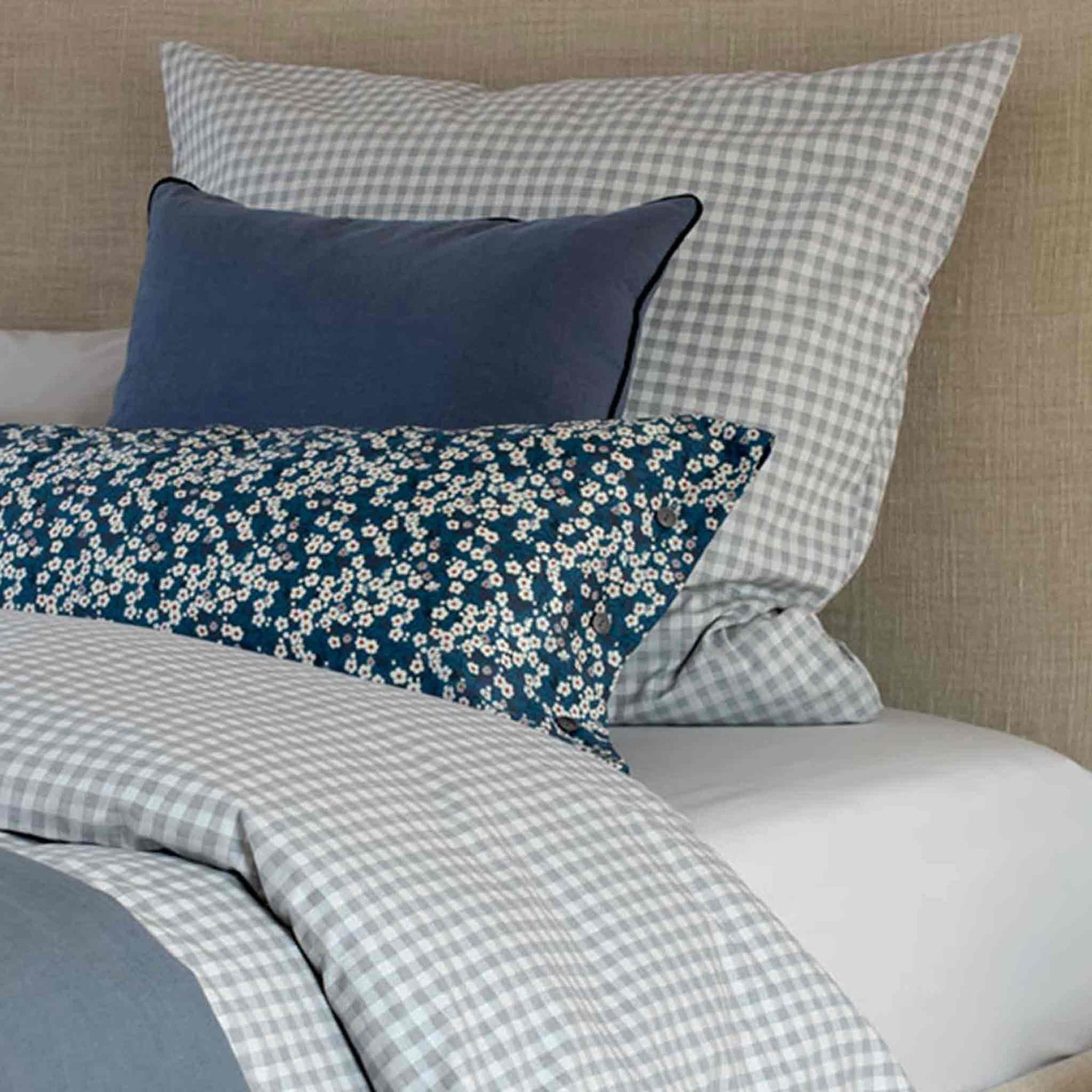 Polster-Bett-mit karierter grau-creme Bettwaesche mit dunkelblauen Leinenkisen und geblümten 40x80 Kissenbezug